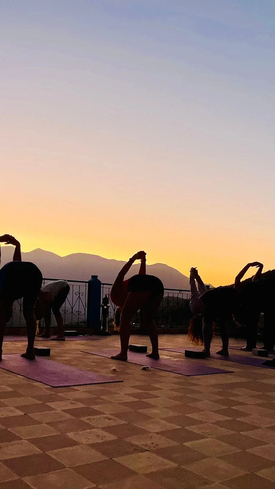Silhouettes of a yoga group stretching against a golden Atlas sunset