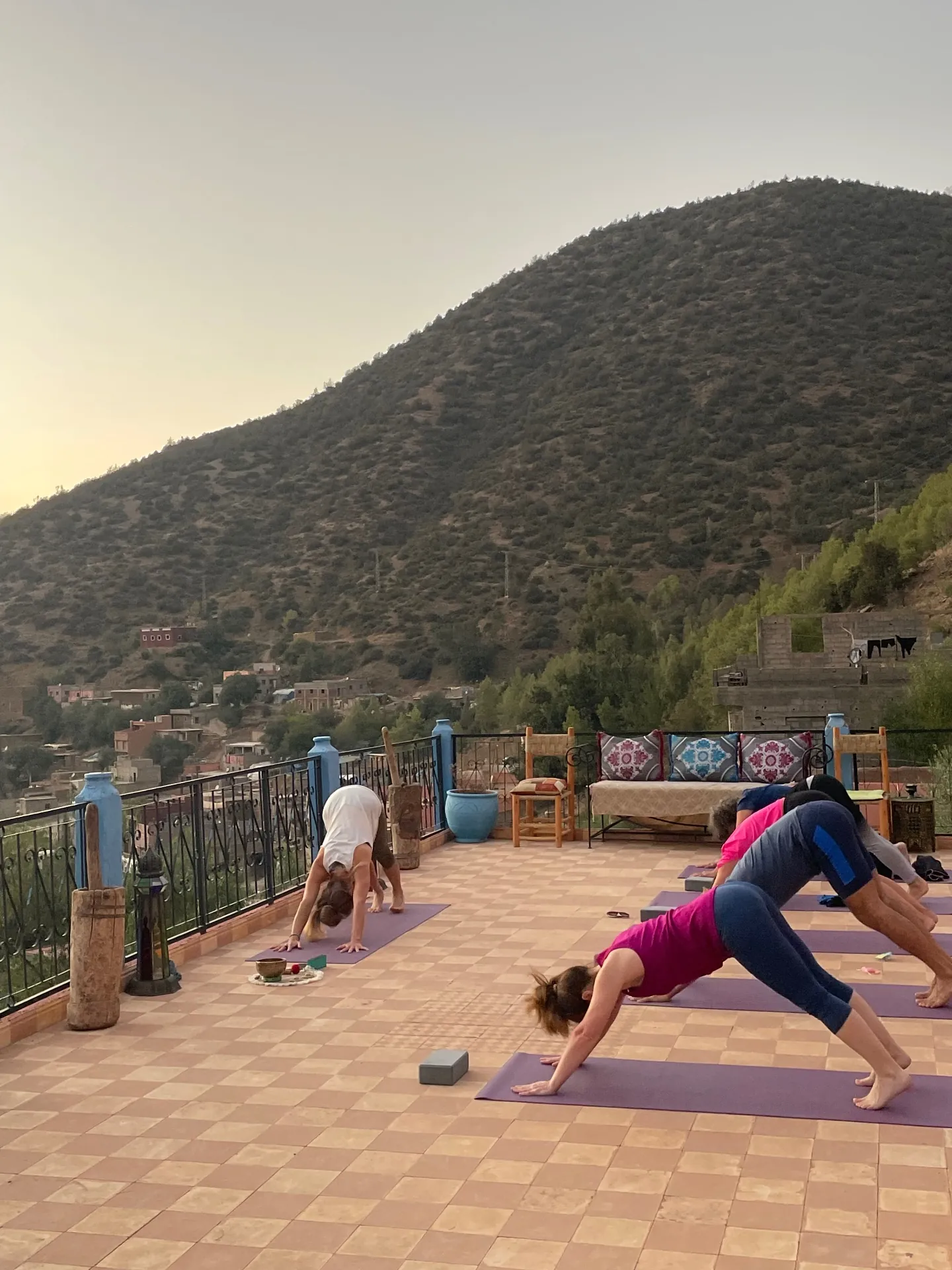 Practitioners in downward dog on the terrace with the mountainside and village behind