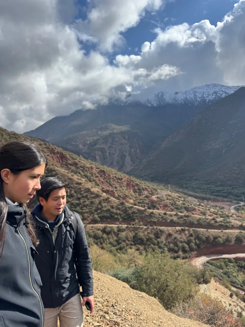 Des marcheurs font une pause au-dessus de la vallée, les cimes enneigées du Haut Atlas en arrière-plan