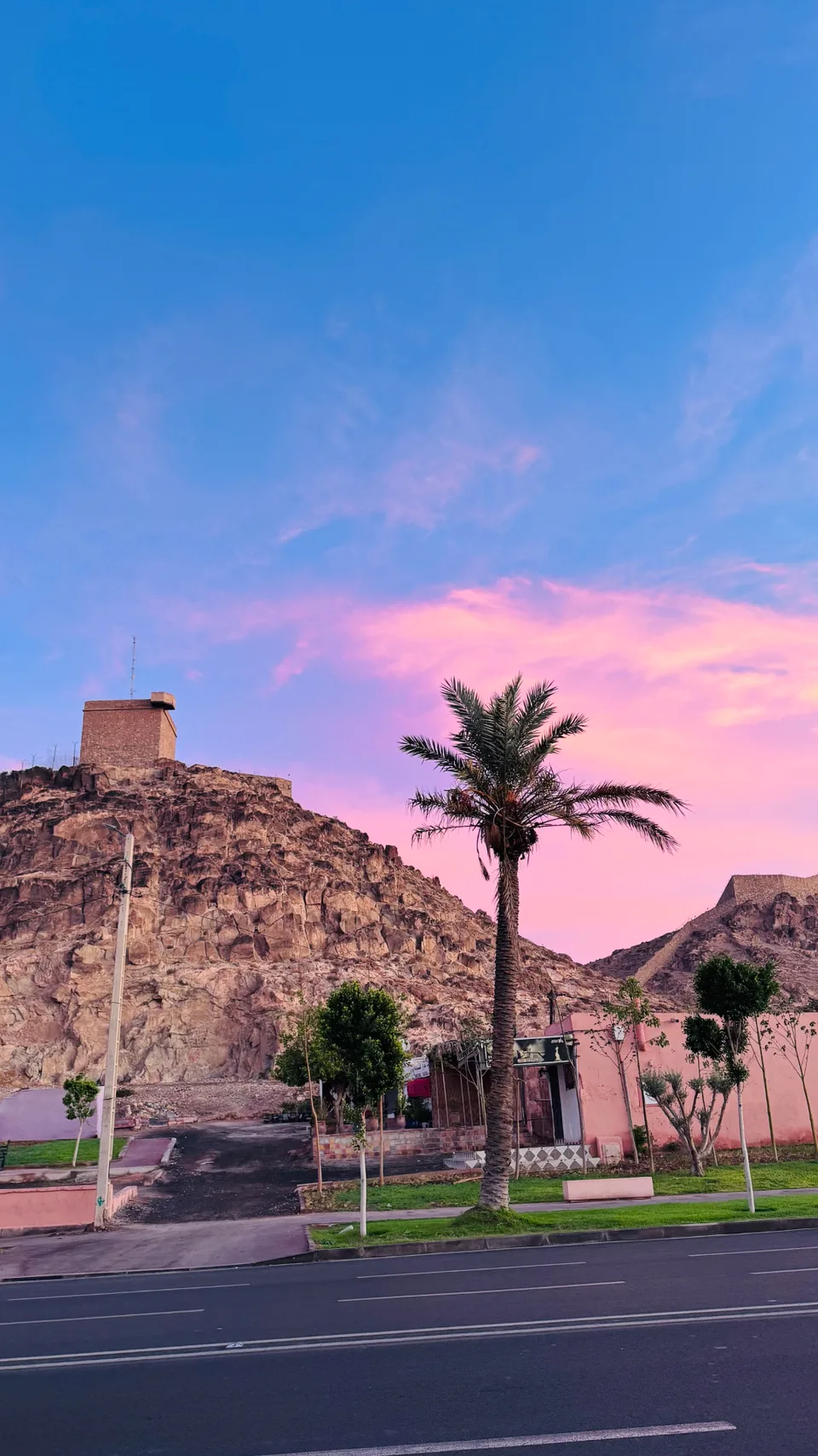 Pink sunset sky over a rocky hilltop watchtower and a lone palm